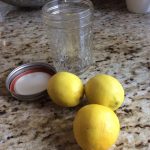 Three lemons and an open glass jar with a lid on a granite countertop.