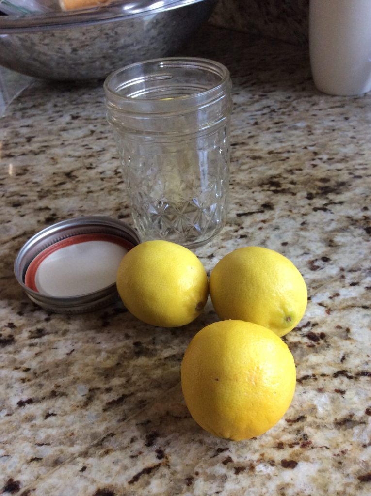 Three lemons and an open glass jar with a lid on a granite countertop.