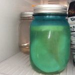 Two jars with metal lids in a refrigerator, one filled with a blue-green liquid.
