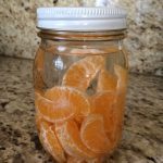 A jar filled with peeled mandarin orange segments on a granite countertop.
