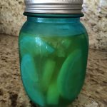 A blue mason jar filled with sliced pickles, placed on a granite countertop.
