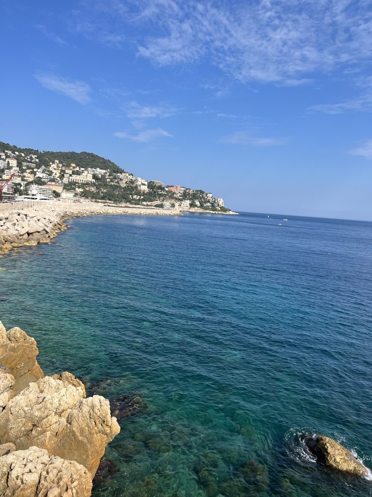 Coastal view with rocky shoreline and clear blue water under a partly cloudy sky.