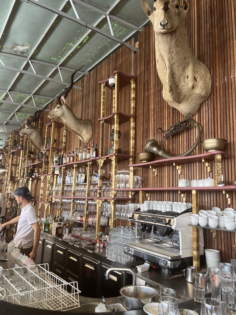 Bar interior with taxidermy deer heads mounted on a wooden wall, glassware, liquor bottles, and an espresso machine behind the counter.
