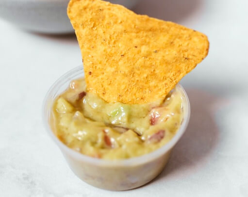 Tortilla chip dipped in guacamole in a small plastic cup.