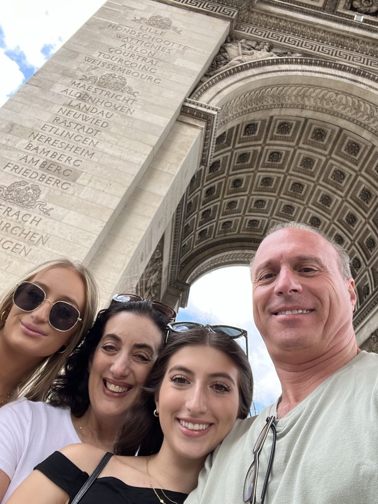 A group of four people smiling in front of the Arc de Triomphe in Paris.