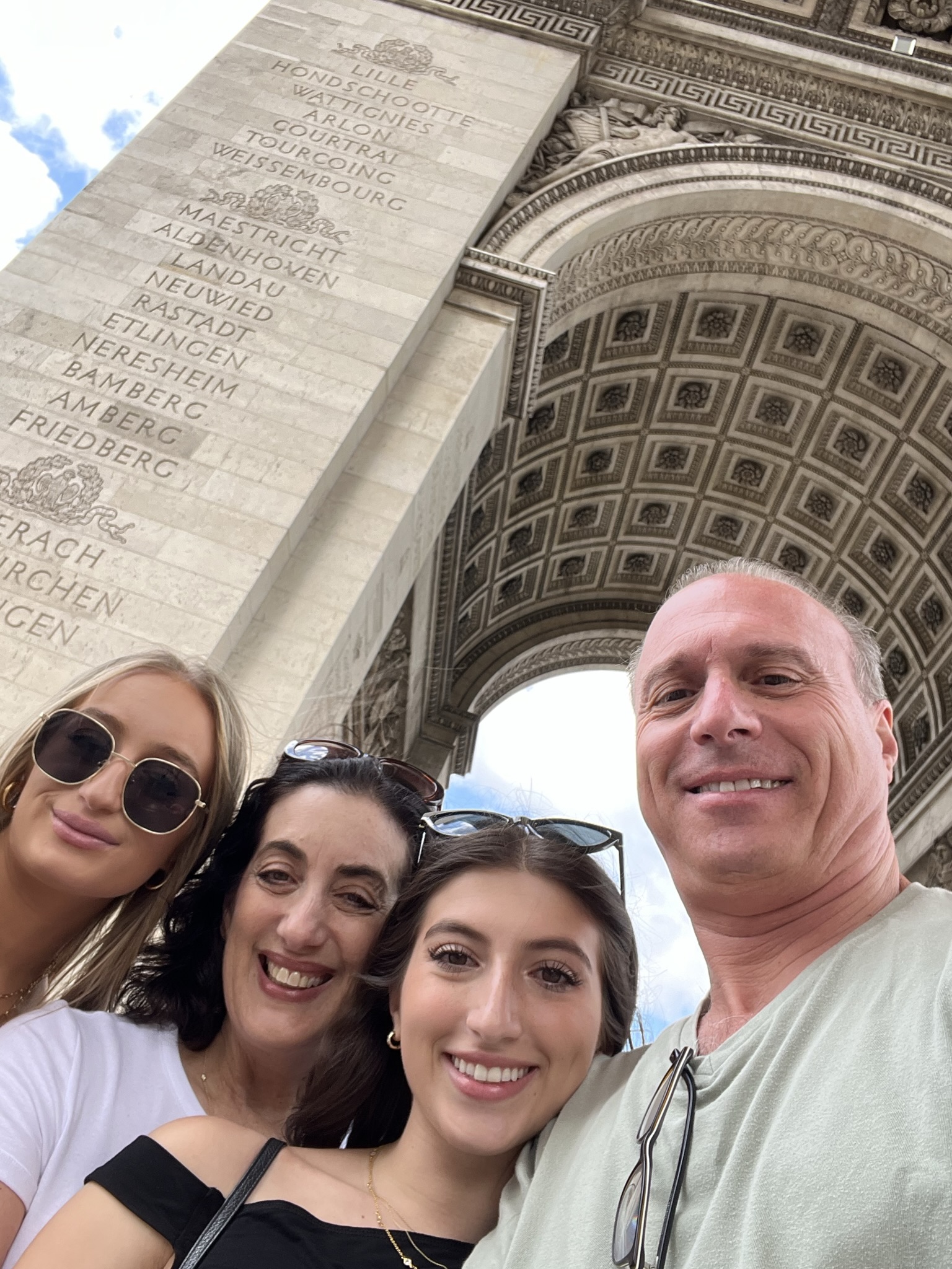 A group of four people smiling in front of the Arc de Triomphe in Paris.