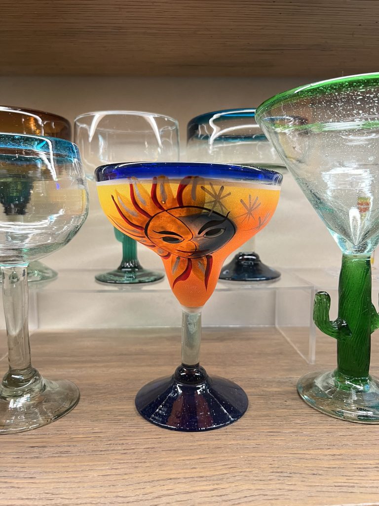 Colorful margarita glass with a sun and moon design on the bowl, surrounded by other decorative glasses.