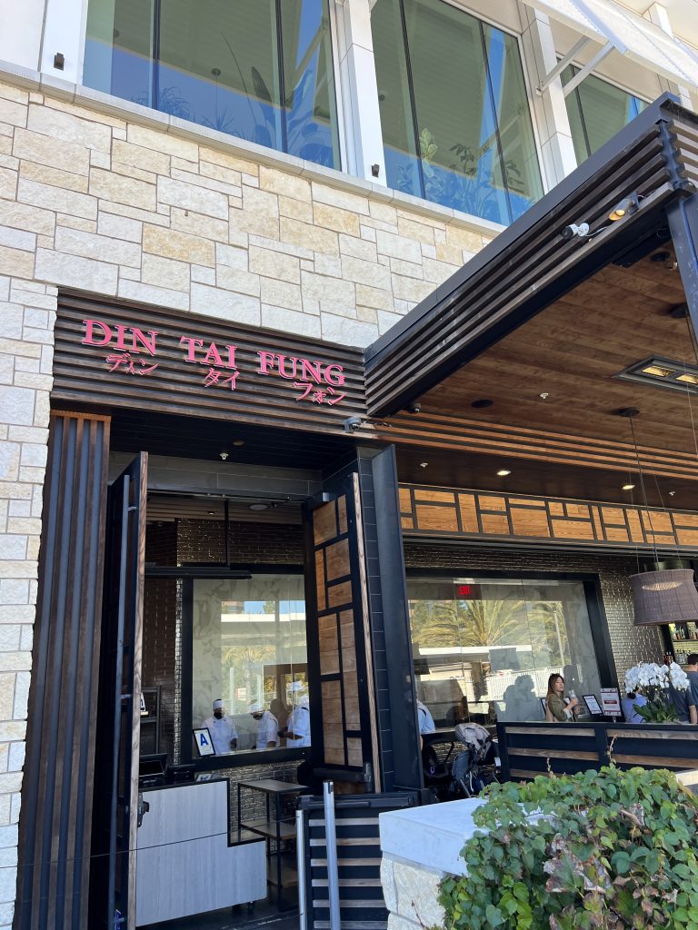 Entrance of a Din Tai Fung restaurant with open glass doors, showing staff and customers inside.