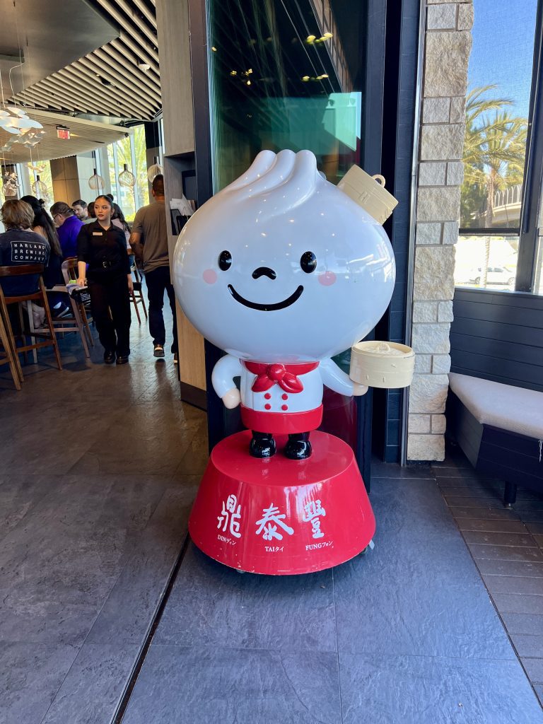 Cute dumpling mascot statue inside a restaurant, holding a bamboo steamer basket.