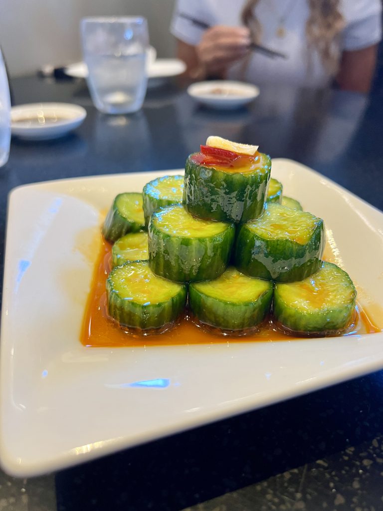 A plate of sliced cucumbers stacked in a pyramid, drizzled with orange sauce, and garnished with red peppers.