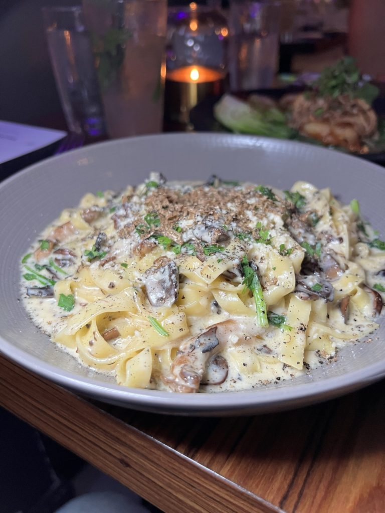 A plate of creamy mushroom pasta garnished with herbs, served on a wooden table with dim lighting and a candle in the background.