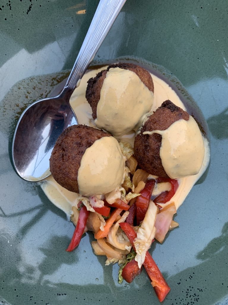 Three falafel balls with creamy sauce and vegetable garnish in a green bowl with a spoon.