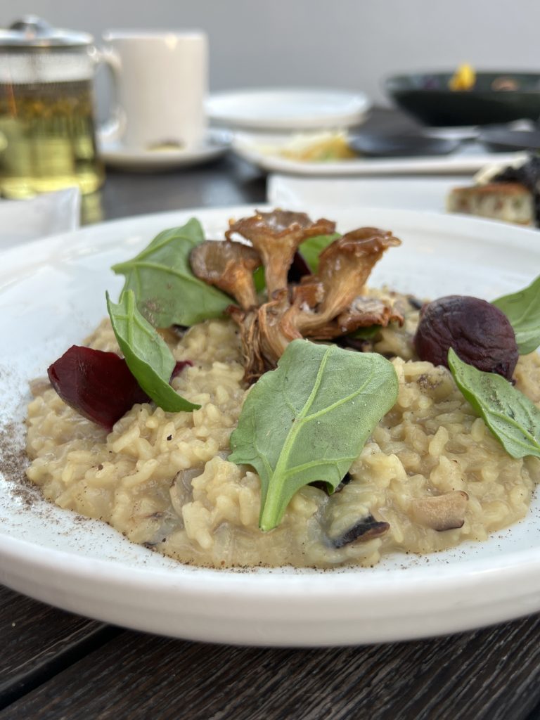A plate of mushroom risotto garnished with greens and roasted mushrooms, on a wooden table.