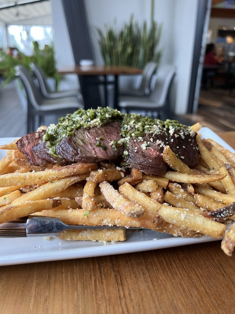 Steak topped with chimichurri sauce served on a bed of seasoned fries.