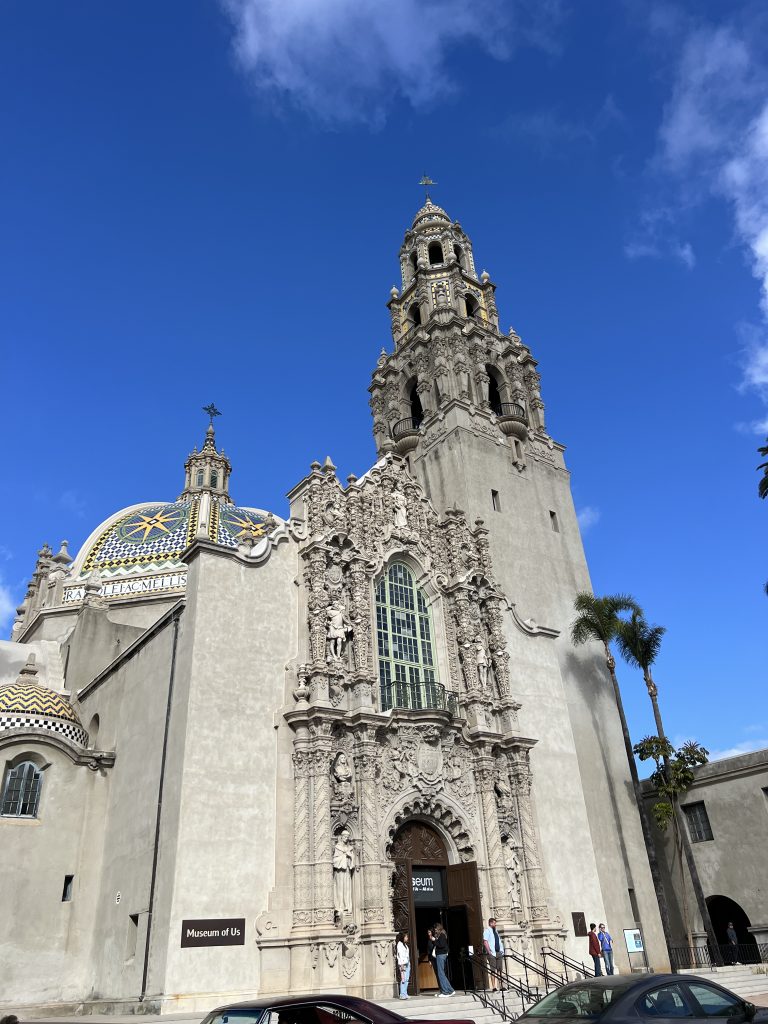 Ornate historical building facade with a tall bell tower and intricate stone carvings under a bright blue sky.