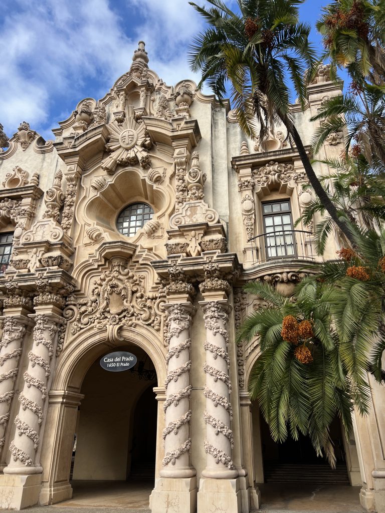 Ornate façade of Casa del Prado with intricate carvings and spiral columns, framed by palm trees against a blue sky.