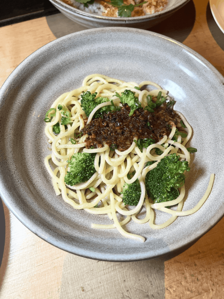 A bowl of spaghetti with broccoli and a dark sauce on a ceramic plate.