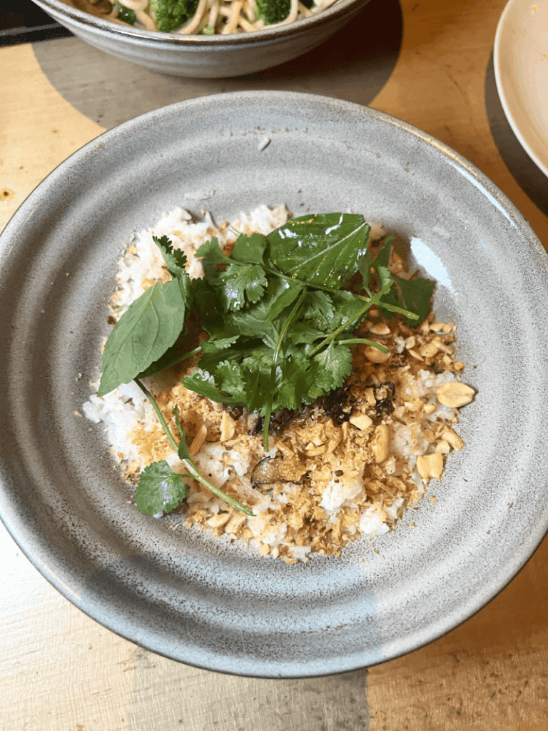A bowl of rice topped with fresh herbs, crushed peanuts, and crispy fried onions.