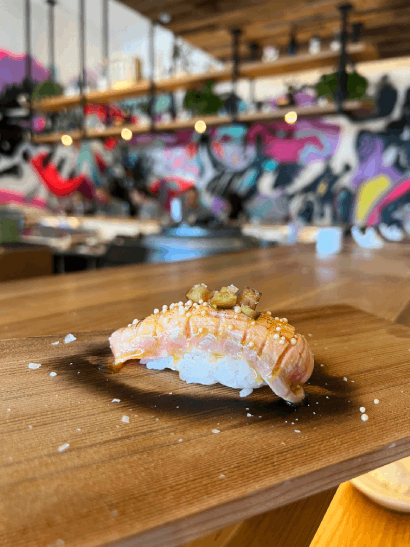 A piece of intricate sushi placed on a wooden table in a stylish, colorful restaurant interior.