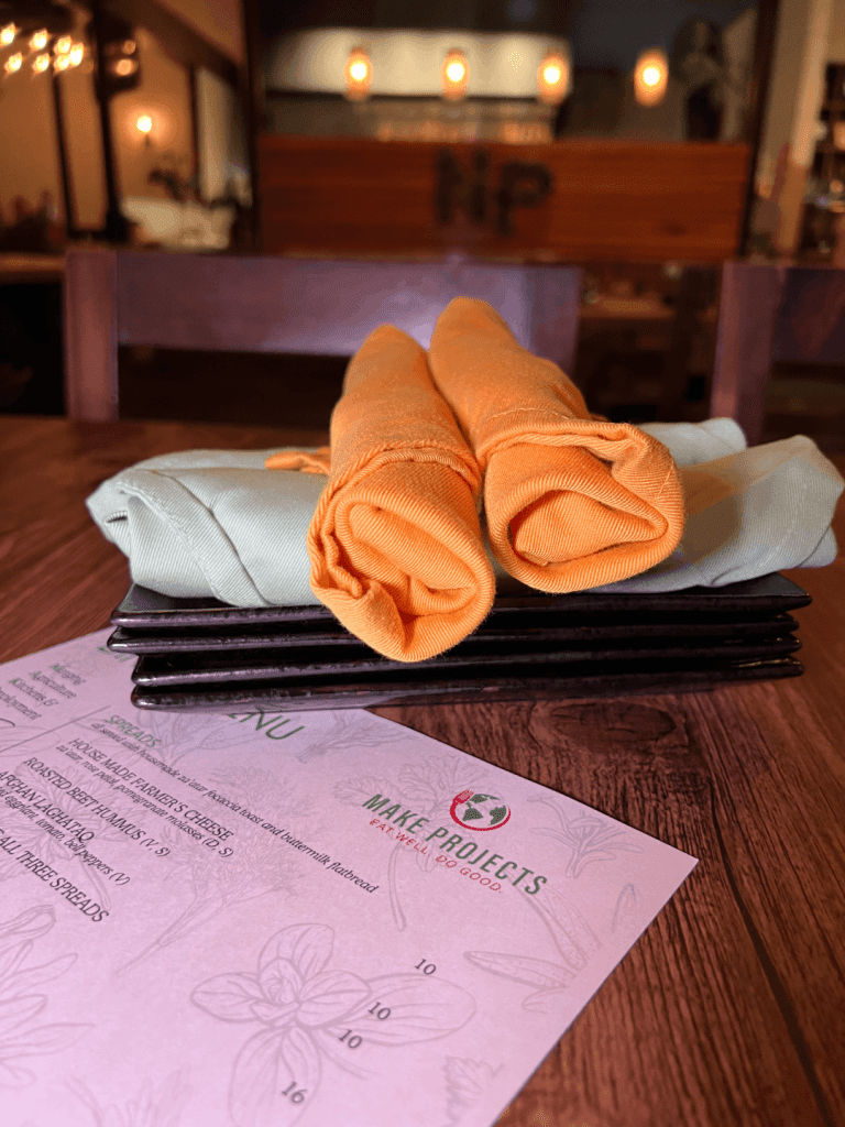 Folded orange napkins on stacked plates with a menu on the table in a restaurant setting.
