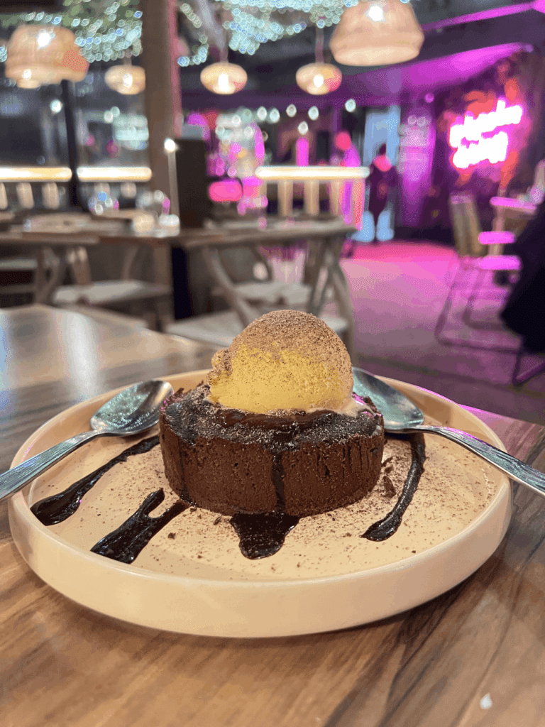 Chocolate dessert with a scoop of vanilla ice cream and chocolate drizzle on a plate, set in a warmly lit restaurant.