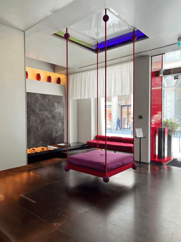 A modern interior with a suspended purple cushion swing, a lounge seating area, and large windows.