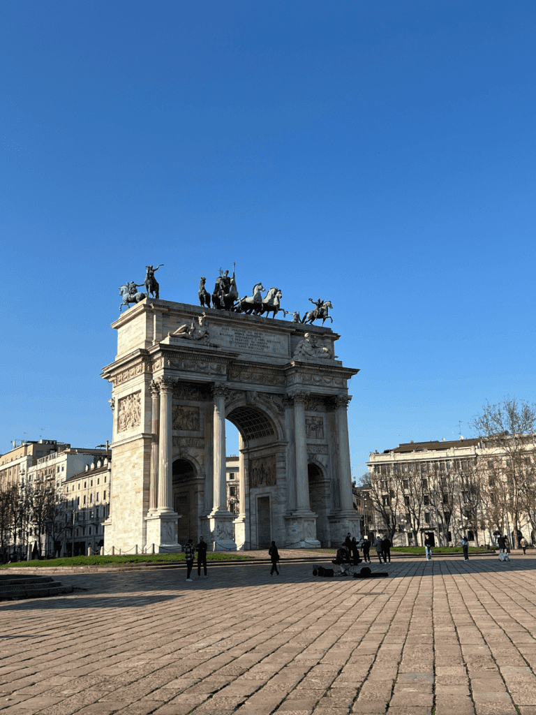 Arch of Peace in Milan, Italy, under a clear blue sky with people walking nearby.
