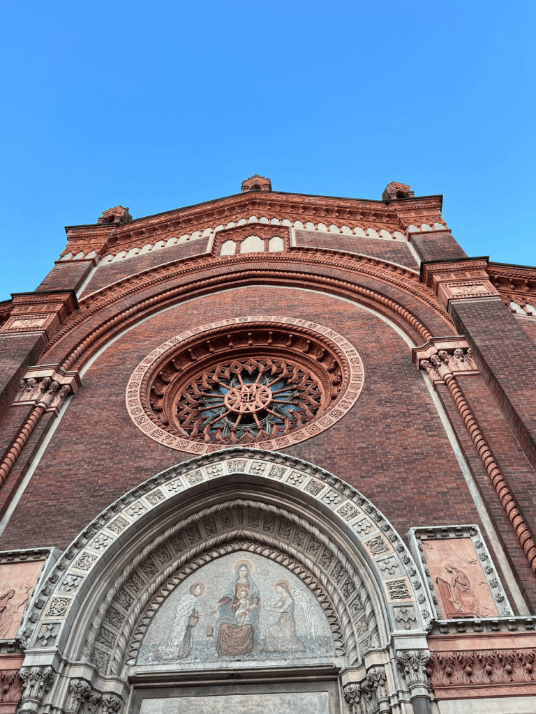 Facade of a brick Gothic-style church with ornate arch and circular stained glass window.