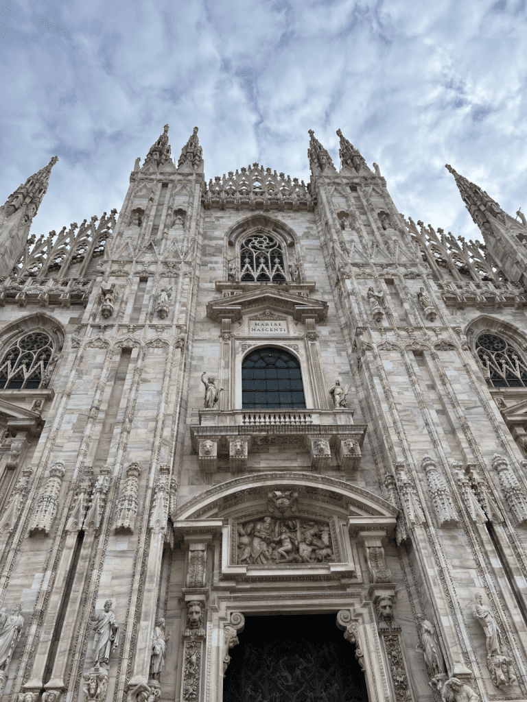 Facade of a Gothic cathedral with ornate carvings and spires under a cloudy sky.