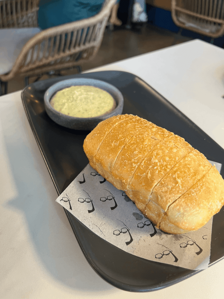 A loaf of sliced bread served on a dark platter with a small bowl of creamy dip.