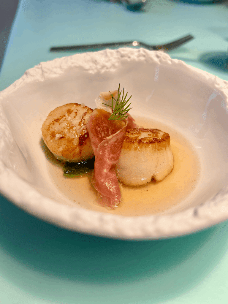 Seared scallops with prosciutto and garnish in a white bowl.