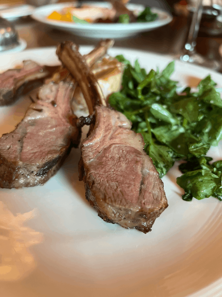 A plate of cooked lamb chops with greens on the side.