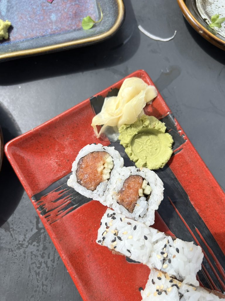 Sushi rolls with a side of wasabi and pickled ginger on a red plate.