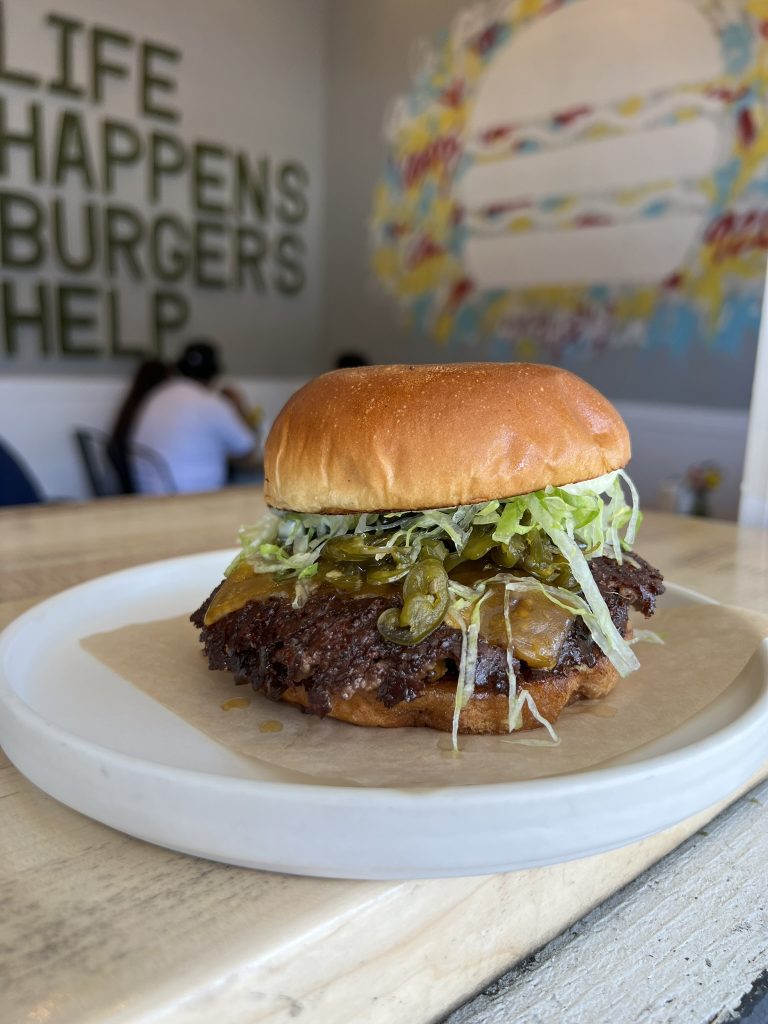 A burger with lettuce, jalapeños, and melted cheese on a bun, served on a white plate.
