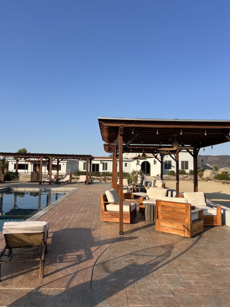 Outdoor patio with wooden furniture and a pool under a clear blue sky.