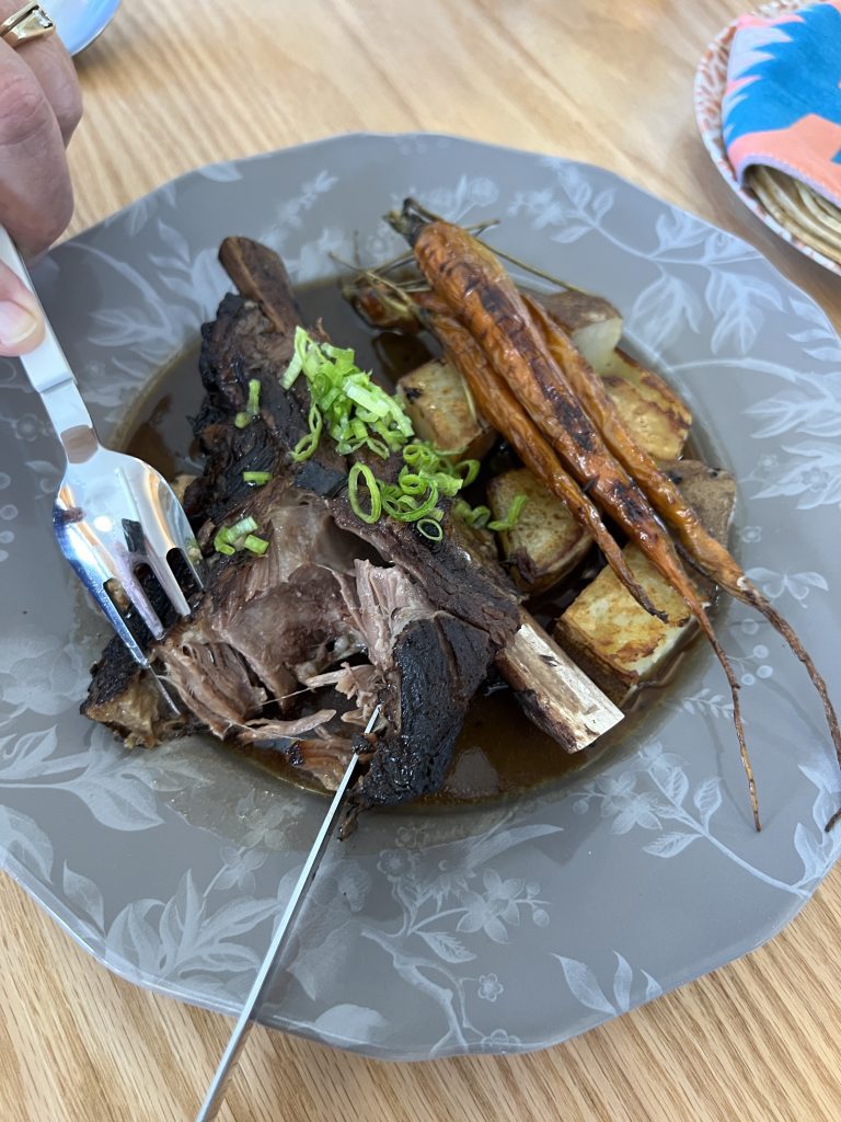 A plate of braised short ribs with roasted carrots, potatoes, and green onions.