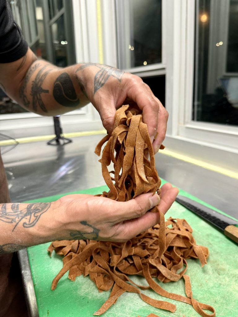 Person holding freshly made brown pasta strips over a green cutting board.