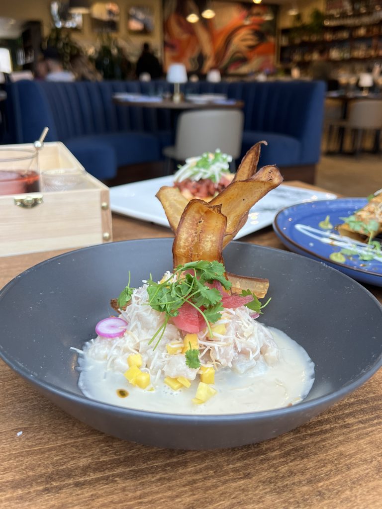 A bowl of ceviche topped with herbs and plantain chips on a restaurant table.
