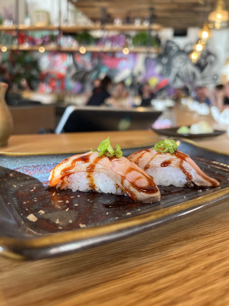 Two pieces of sushi with a drizzle of sauce on a plate in a restaurant setting.
