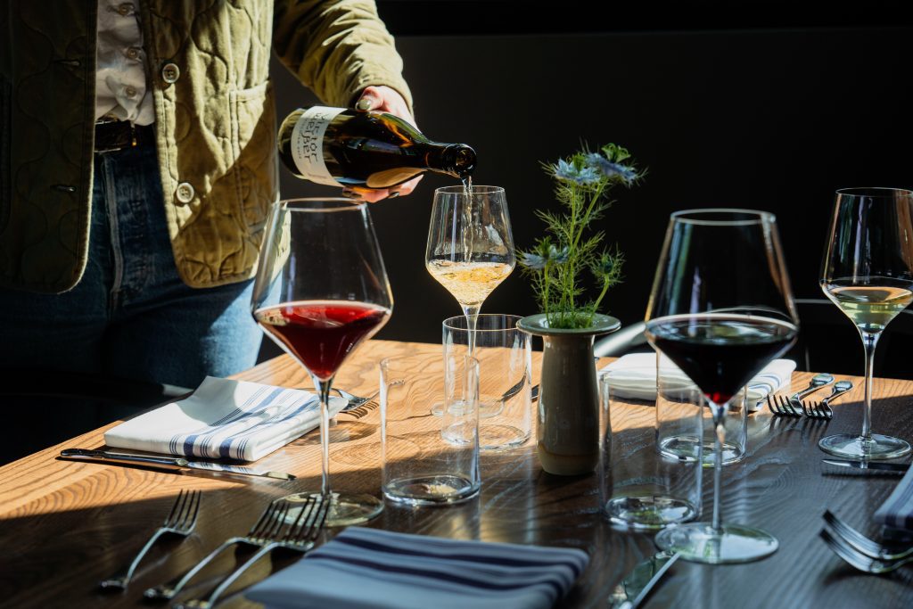 Person pouring wine into a glass at a set dining table with flowers.