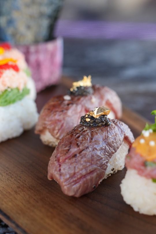 Close-up of a platter with gourmet sushi, including pieces topped with seared beef, caviar, and gold leaf.